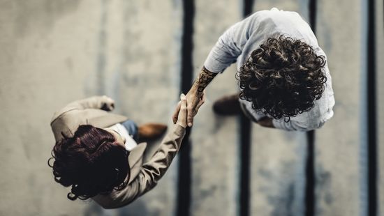 Kameraperspektive von oben: Ein Mann und eine  Frau schütteln sich die Hand. Foto: © nimis69/E+/Getty Images 