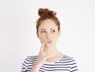 Find a degree programme: Young woman with pinned-up hair ponders and taps her cheek with her index finger. Photo: © Gpoint Studio/Getty Images/iStockphoto